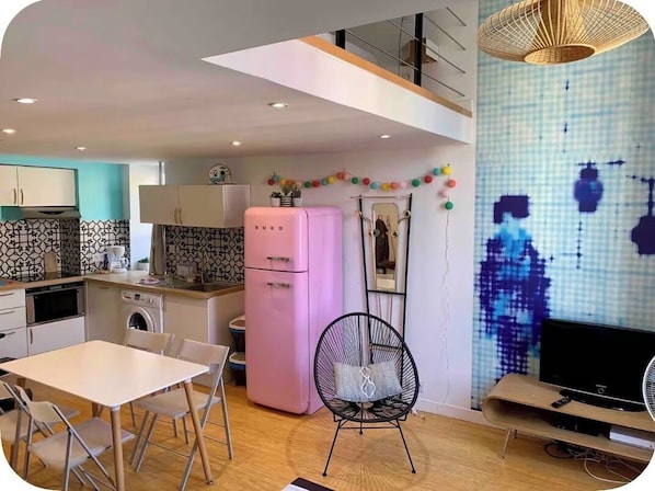 Une cuisine moderne avec un coin repas, un réfrigérateur rose et un téléviseur à écran plat.