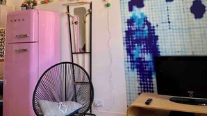 Een moderne woonkamer met een roze koelkast, een zwarte stoel, een televisie en een bijzonder kunstwerk aan de muur.