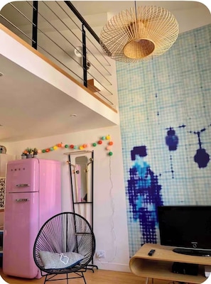 Ein modernes Wohnzimmer mit einem pinkfarbenen Kühlschrank, einem schwarzen Sessel, einem Fernseher und einem außergewöhnlichen Wandkunstwerk.