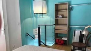 Een slaapkamer met een bed, nachtkastje, lamp, plank met opbergdozen, en een kledingkast.