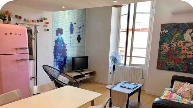 Een compacte woonruimte met een eethoek, een kitchenette, een televisie en een groot raam dat voor natuurlijk licht zorgt.