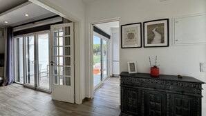 Un'ampia stanza con una grande porta scorrevole in vetro che si apre su un'area esterna, un mobile contenitore in legno scuro con elementi decorativi e due quadri con citazioni motivazionali appesi al muro.