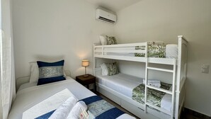 Una camera d'albergo con un letto a castello, un letto singolo, un comodino con una lampada e un condizionatore d'aria a parete.