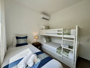 Ein Hotelzimmer mit Etagenbett, einem Einzelbett, einem Nachttisch mit Lampe und einer Klimaanlage an der Wand.