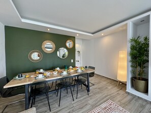 Ein Essbereich mit einem langen Tisch, Stühlen und einer grünen Wand mit Spiegeln.