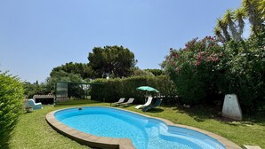 Una piscina con bordo curvo, circondata da un prato curato e un siepe.