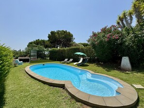 Ein Schwimmbad mit geschwungener Kante, umgeben von einem gepflegten Rasen und einem Heckenstreifen.