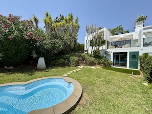 Una casa moderna con piscina, rodeada de exuberante vegetación y palmeras.