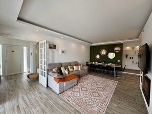 A modern living room with a grey sofa, a dining table, and a TV. - VILAMOURA BROWNS VILLA WITH POOL by HOMING (Vilamoura)