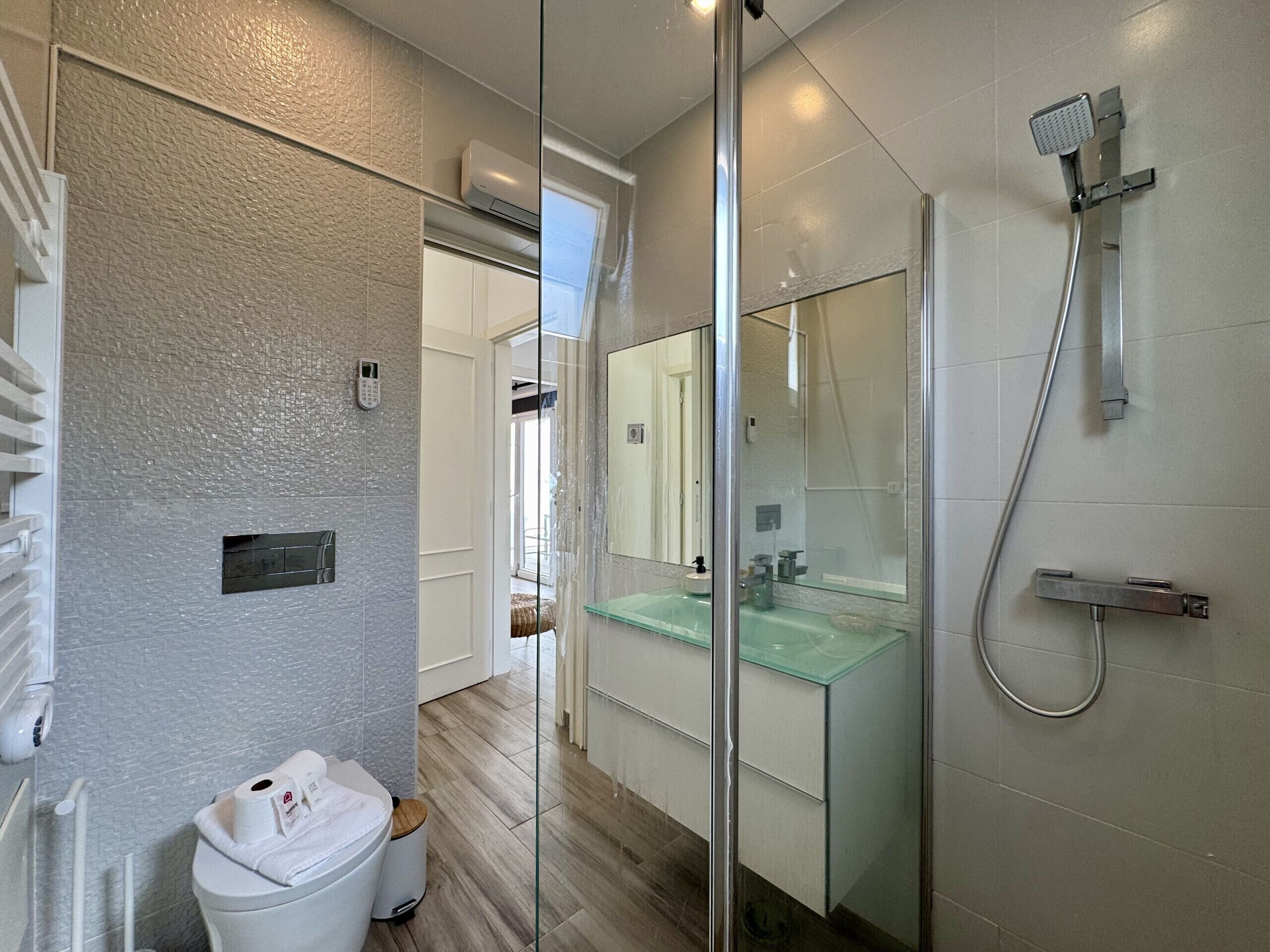 Ein modernes Badezimmer mit einer gläsernen Duschkabine, einem Waschbecken aus Glas und einer Toilette mit weißem Deckel.