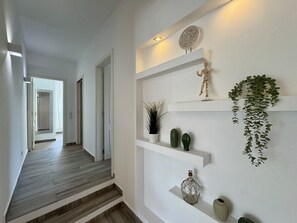 A hallway with a wooden floor, white walls, and a shelf with decorative items including a cactus, a vase, and a hanging plant. - VILAMOURA BROWNS VILLA WITH POOL by HOMING (Vilamoura)