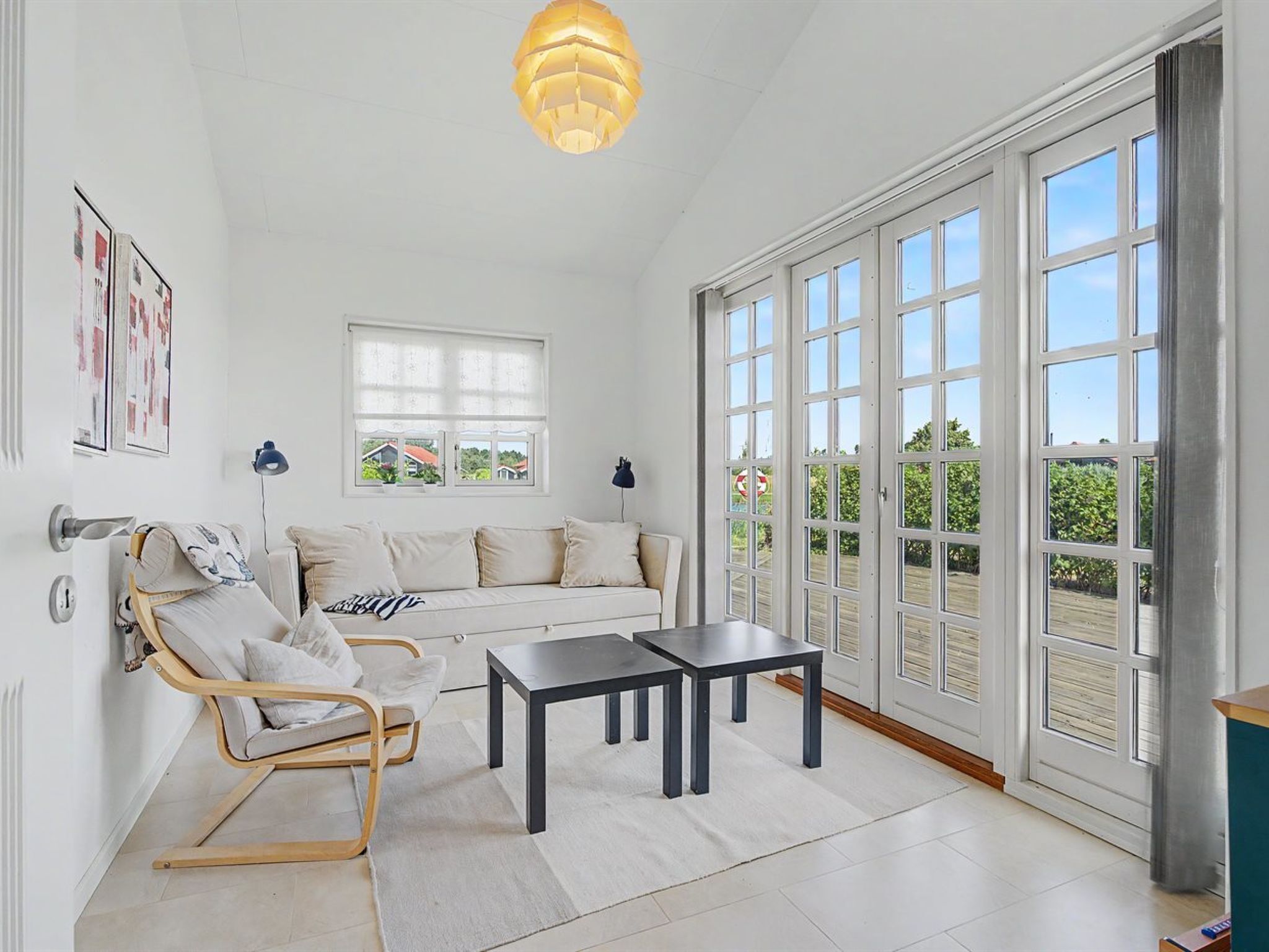 A spacious living room with a sofa, two armchairs, a coffee table, and a large window with a view of greenery.