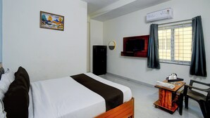 Ein Hotelzimmer mit Bett, Fernseher, Schreibtisch mit Stuhl und einem Fenster mit Vorhängen.
