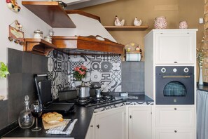 Una cucina con piastrelle a contrasto bianco e nero, un fornello, un lavello e un piano di lavoro con una pagnotta e un bicchiere di vino rosso.