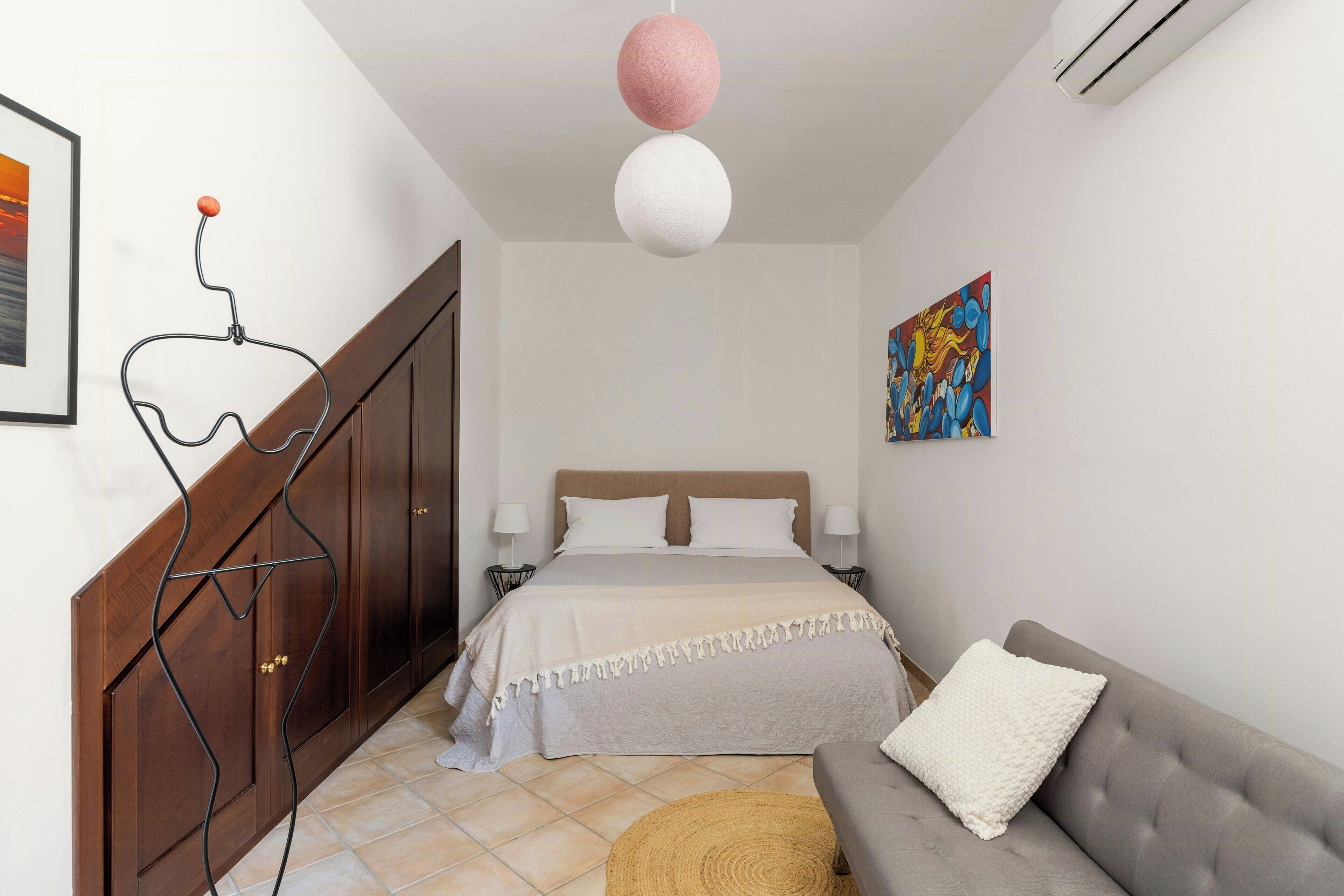 Una camera da letto con un letto, un divano grigio, un quadro e una ventola a soffitto.