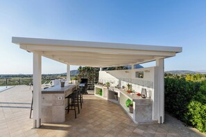 Un'area cucina esterna con una pergola, sgabelli da bar e un barbecue, con vista su un panorama suggestivo.
