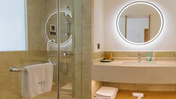 A modern bathroom with a glass-enclosed shower, a round mirror with a light, a sink with toiletries, and a towel rack.