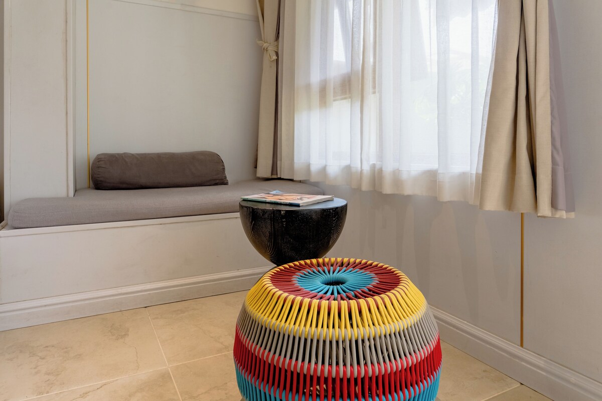 A room with a sofa, a round table, and a colorful stool.