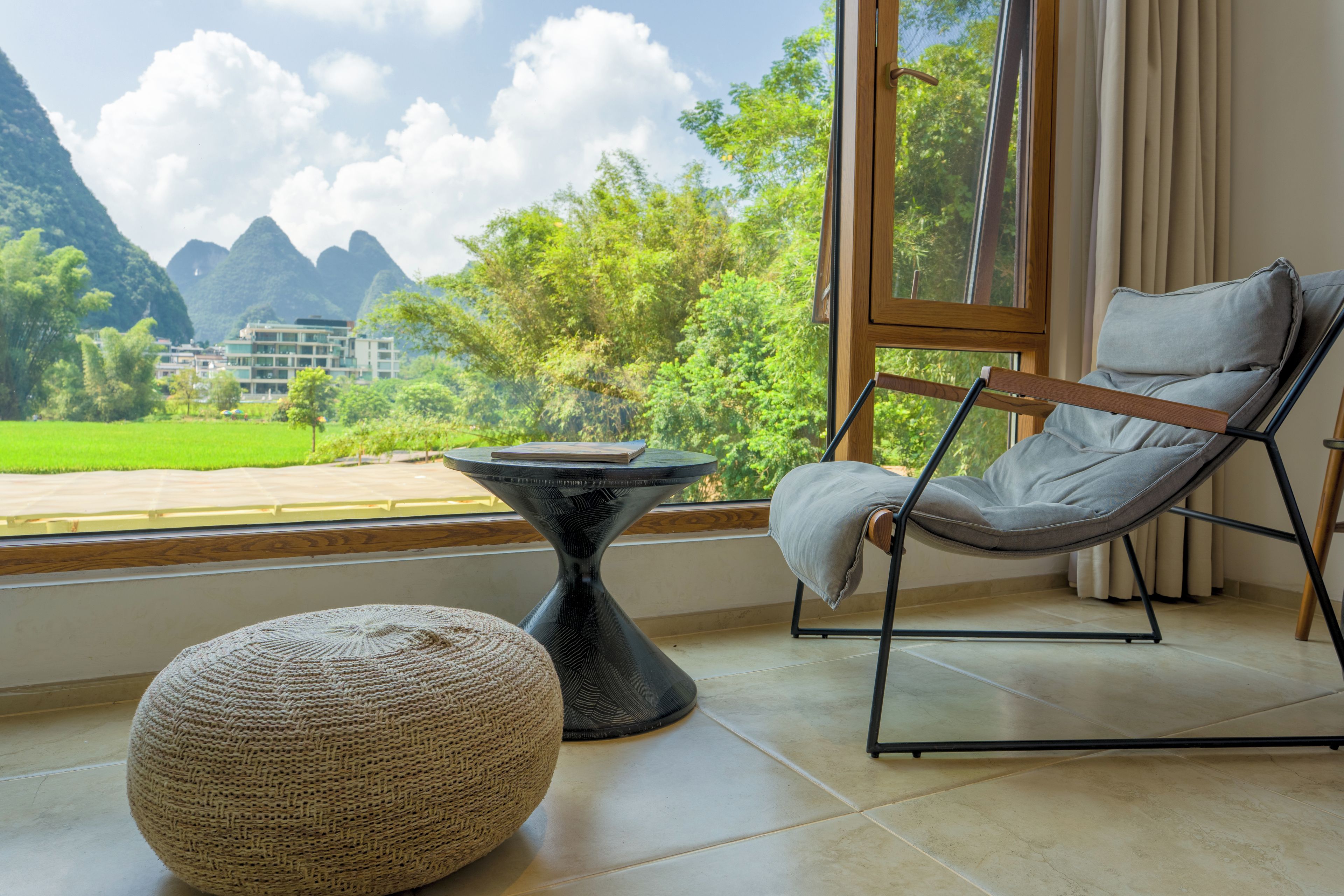 Una habitación con vista a las montañas, una silla, una mesa y un otoman tejido.