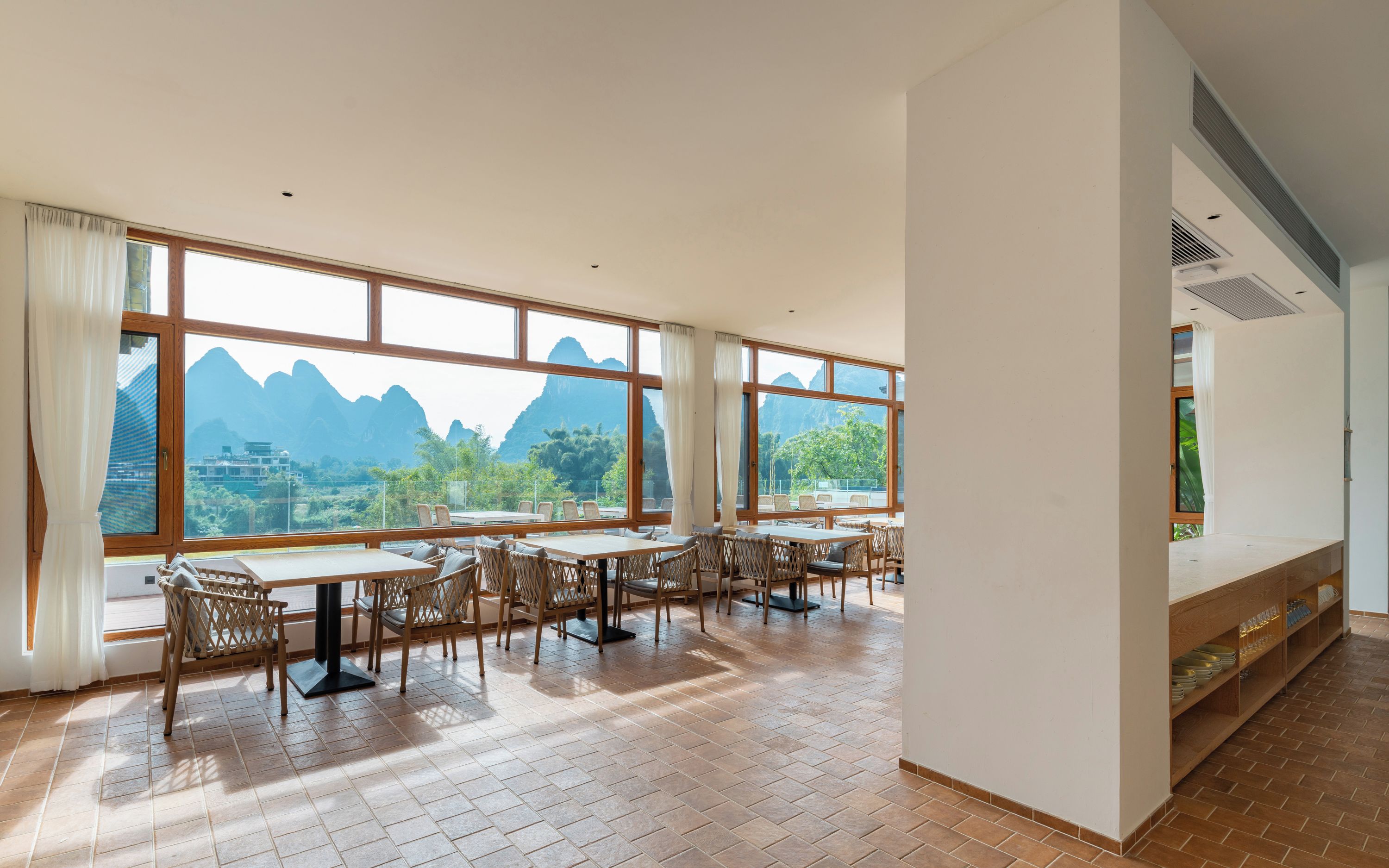 Un espace repas doté de grandes fenêtres, de tables et de chaises en bois.