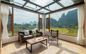A room with a large glass window, a sofa, a chair, and a coffee table. - Yangshuo YueTian Riverside Retreat - Boutique Stay by Yulong River - Talor Made Tours & E-bike Rental (Guilin)
