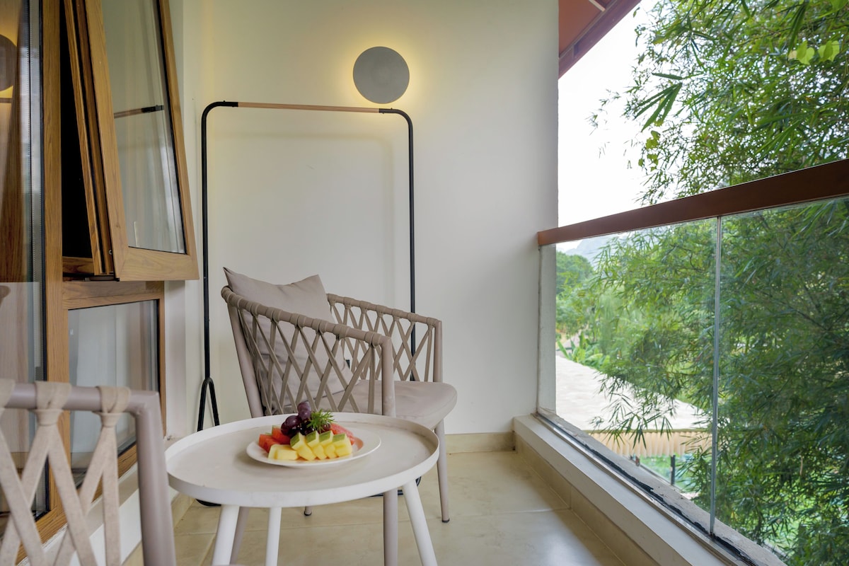 A balcony with a round table, a wicker chair, and a view of greenery.