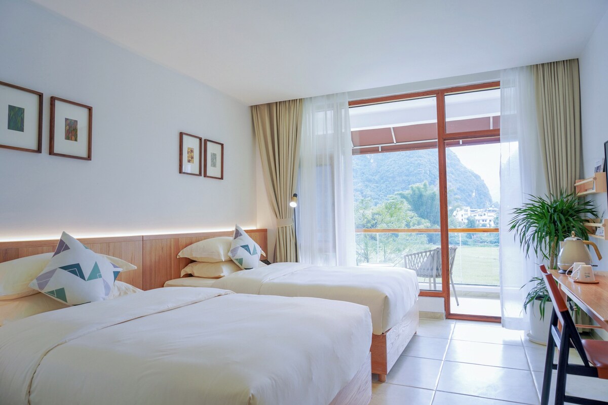 A hotel room with two beds, a balcony with a view of the mountains, and a dining area with a table and chairs.