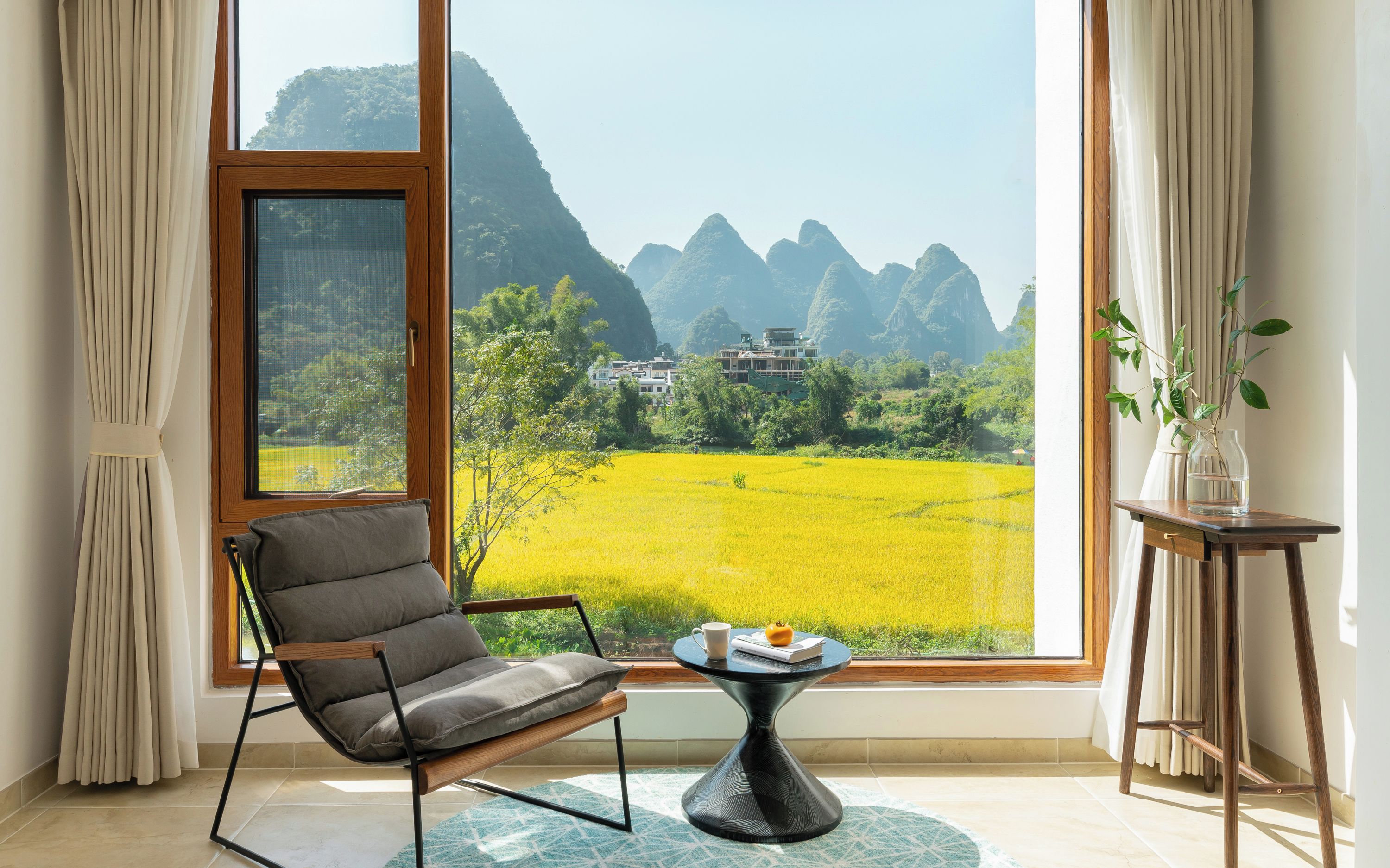 A room with a large window, a chair, a table, and a potted plant.