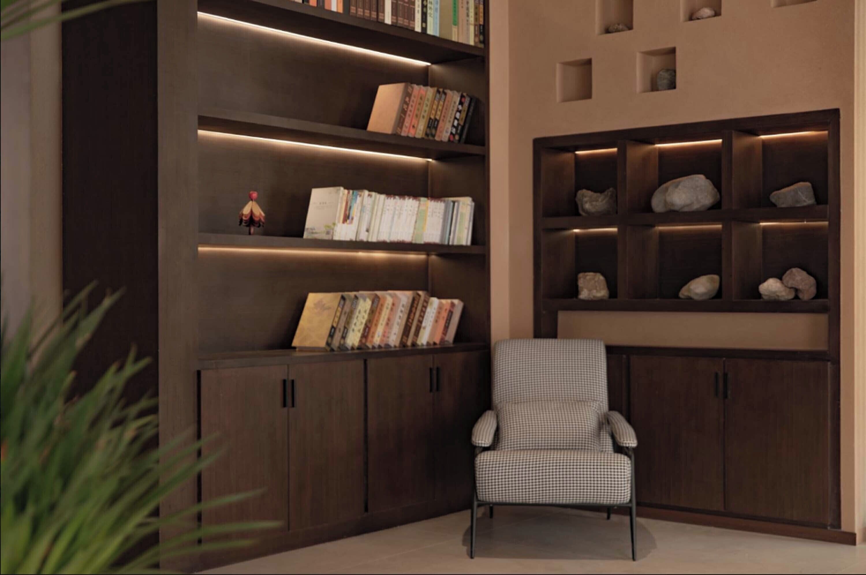 A modern library with dark wood shelving, a checkered armchair, and decorative rocks.