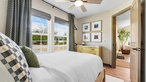 Ein Schlafzimmer mit Bett, Kommode, Deckenventilator und Blick ins Freie.