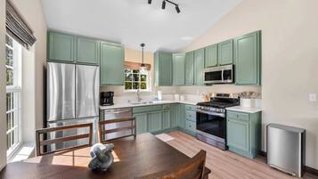 Una cucina moderna con mobili verdi, elettrodomestici in acciaio inossidabile e un'area pranzo con tavolo e sedie in legno.