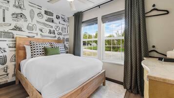 Un dormitorio con una cama de madera, un ventilador de techo, una ventana con cortinas y una pared con papel tapiz de temática náutica.