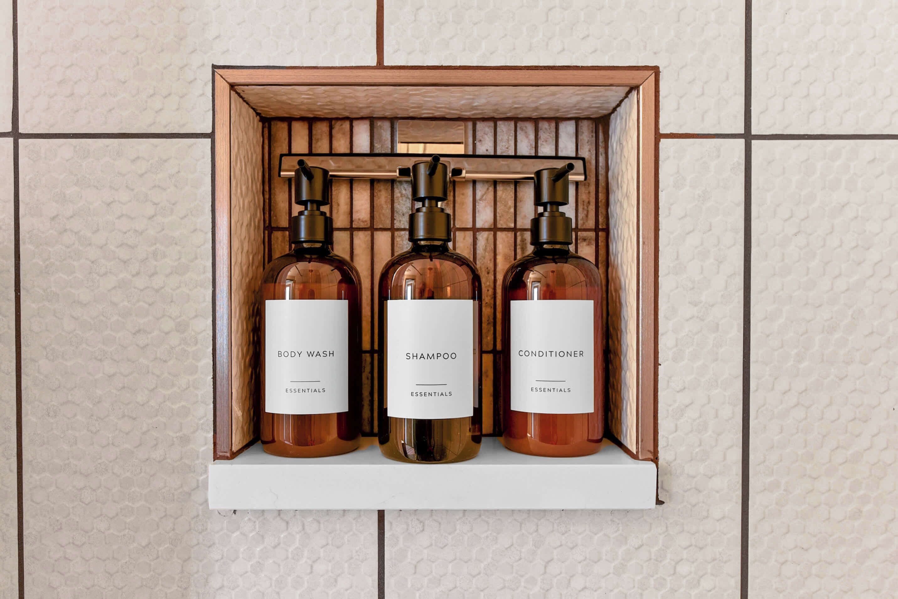 A shelf with three bottles of body wash, shampoo, and conditioner.