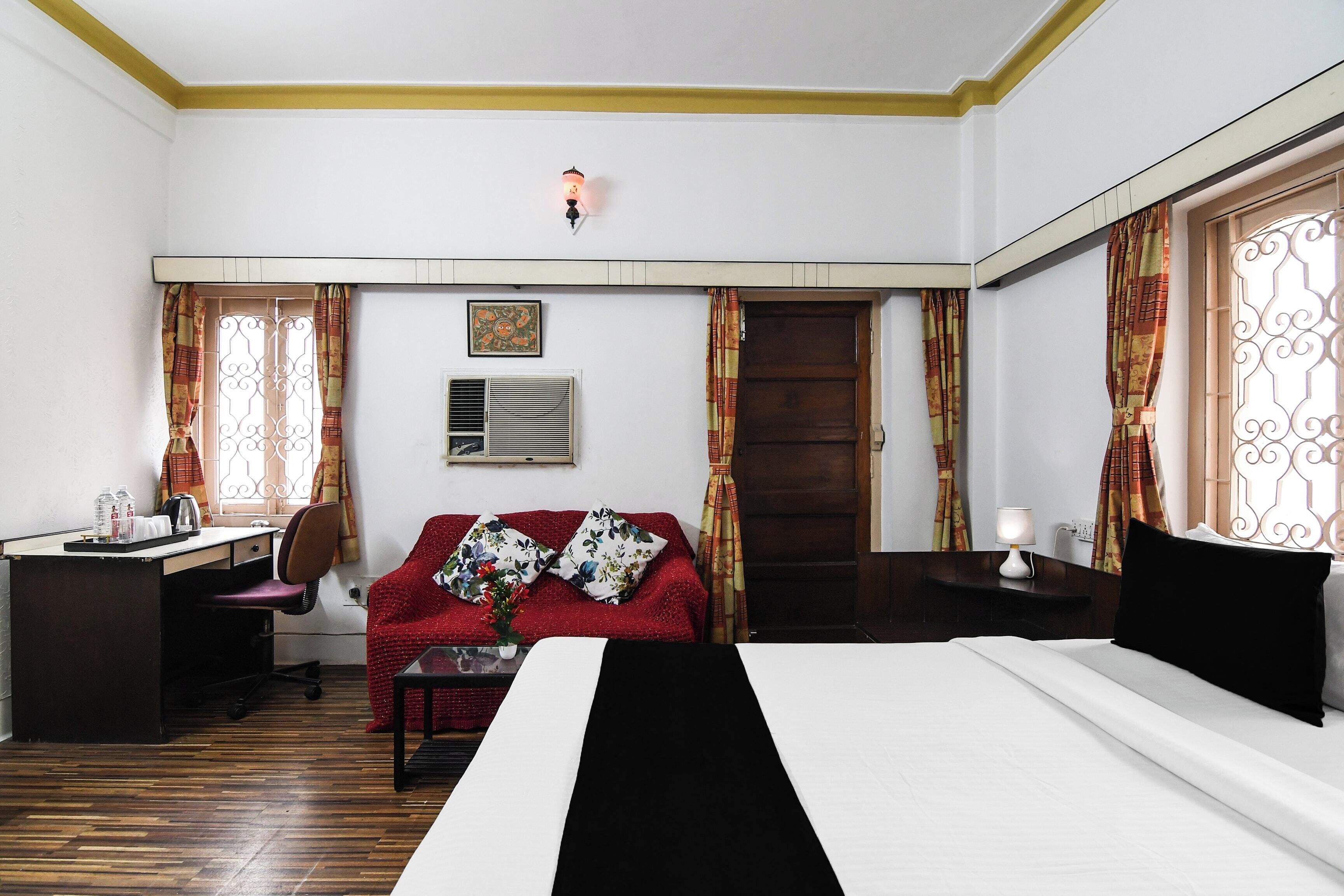 A hotel room with a bed, a desk, a chair, a sofa, and a window with curtains.