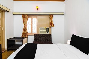 A hotel room with a bed, a small table, a chair, an air conditioning unit, and a window with curtains. - Super Collection O Salt Lake Formerly (Bidhannagar)