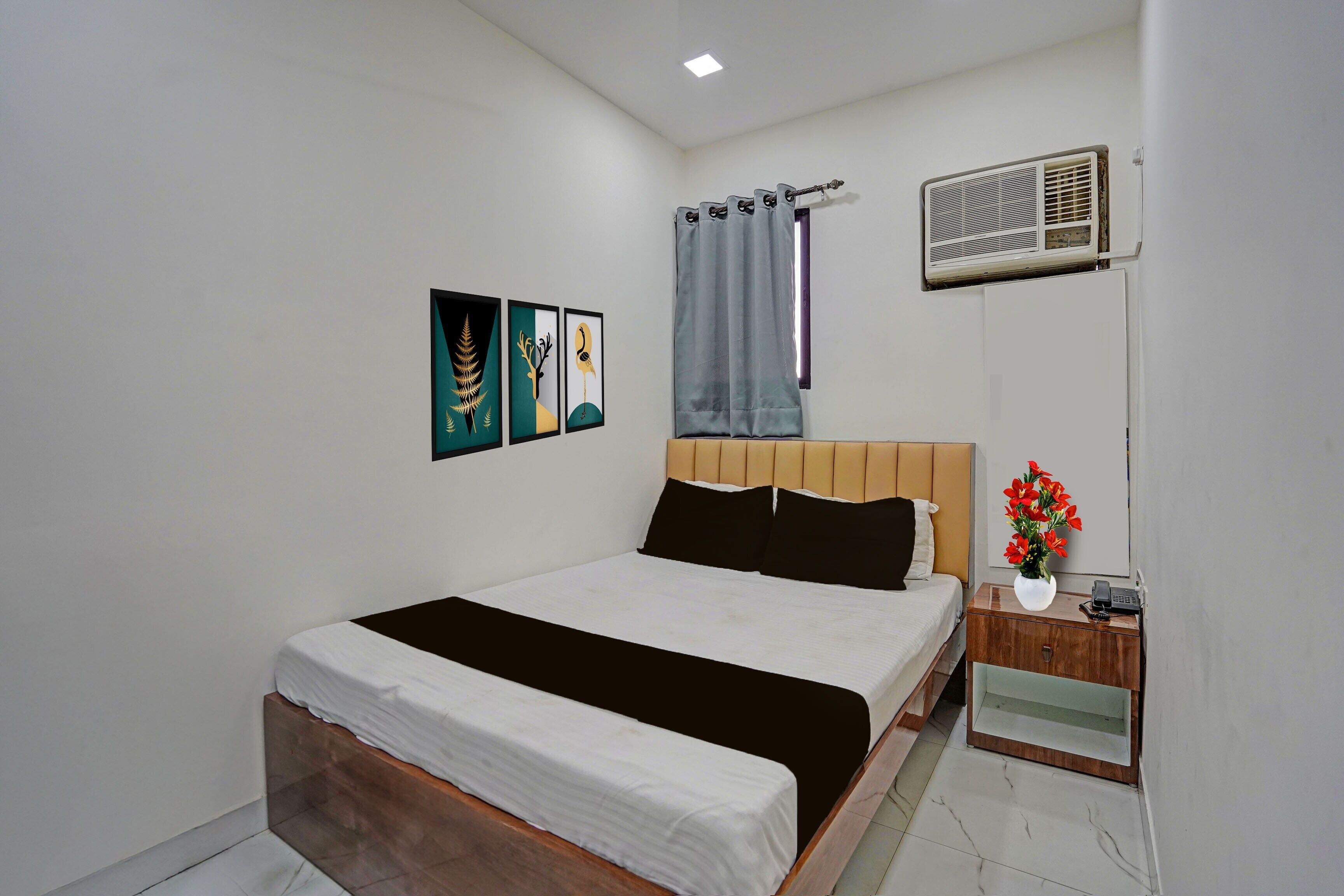 Een slaapkamer met een bed, nachtkastje, een luchtverkoeler aan de muur en drie kunstwerken in lijsten.
