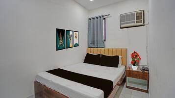 Een slaapkamer met een bed, nachtkastje, een luchtverkoeler aan de muur en drie kunstwerken in lijsten.