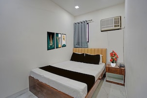 Un dormitorio con cama, mesita de noche, aire acondicionado de pared y tres obras de arte enmarcadas.