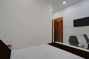 A bedroom with a bed, a wooden door, a television mounted on the wall, and a chair. - CollectionO Bisarjan Ghat (Baruipur)