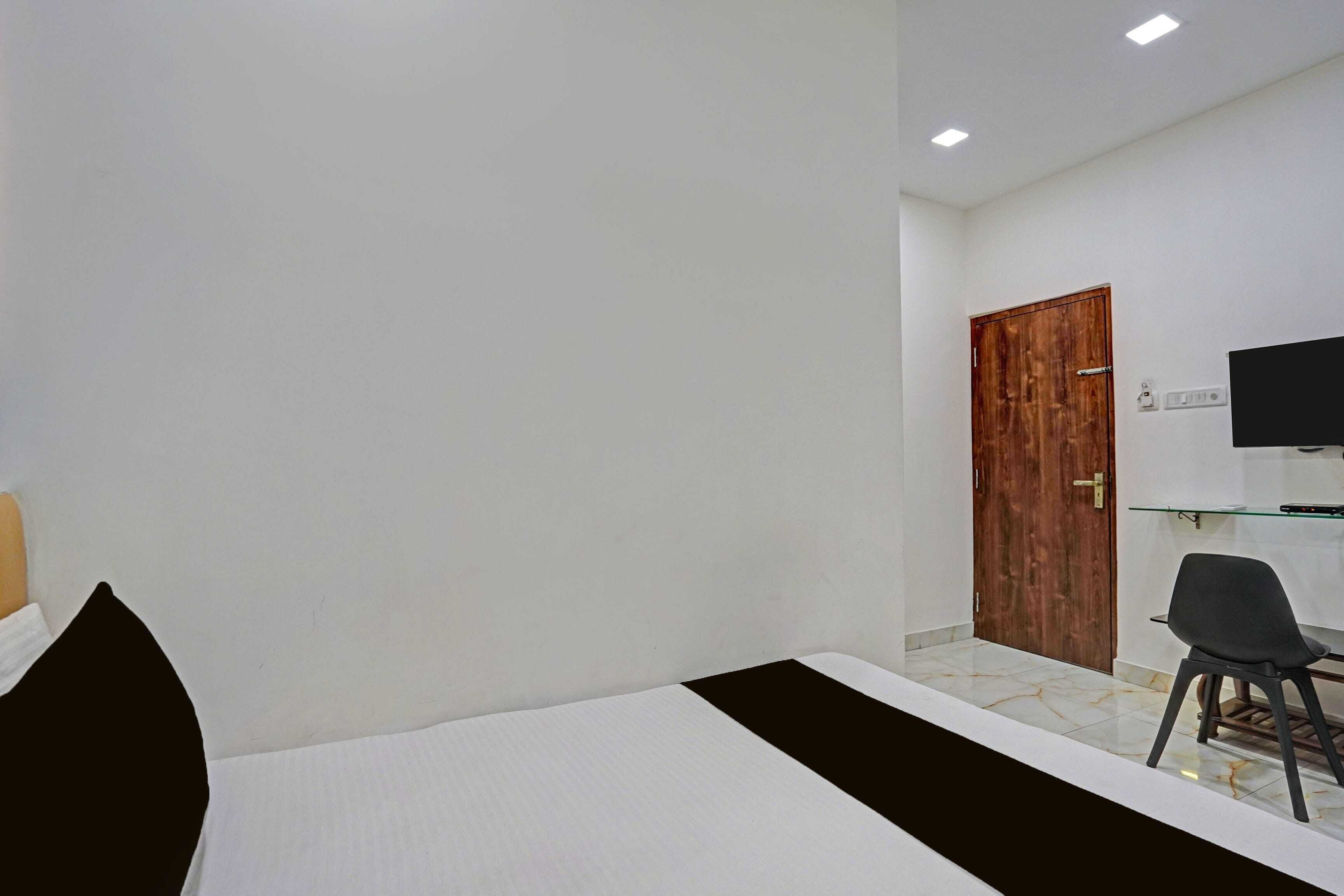 A hotel room with a bed, a desk, a chair, a wooden door, and a flat-screen TV.