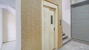 Une porte d’ascenseur fermée dotée d’un écran numérique, un escalier menant à une porte métallique fermée par un volet, et un mur à texture.