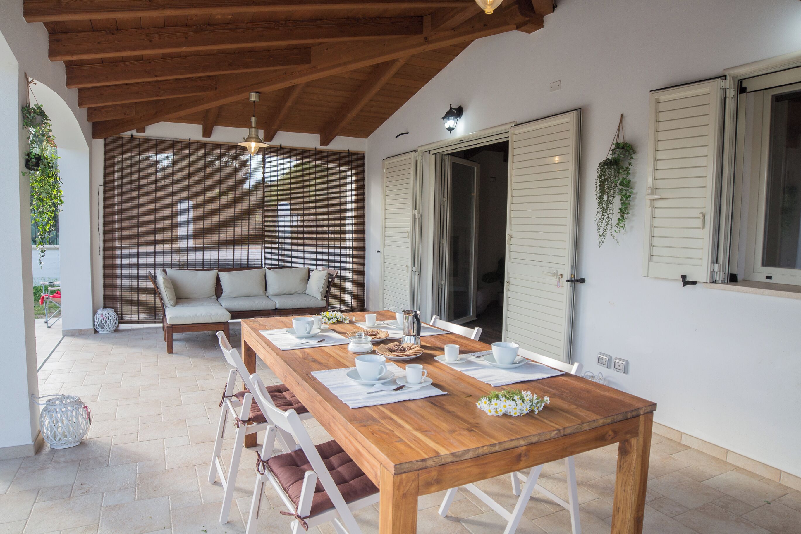 A dining area with a wooden table set for four, a sofa, and a view through a door.