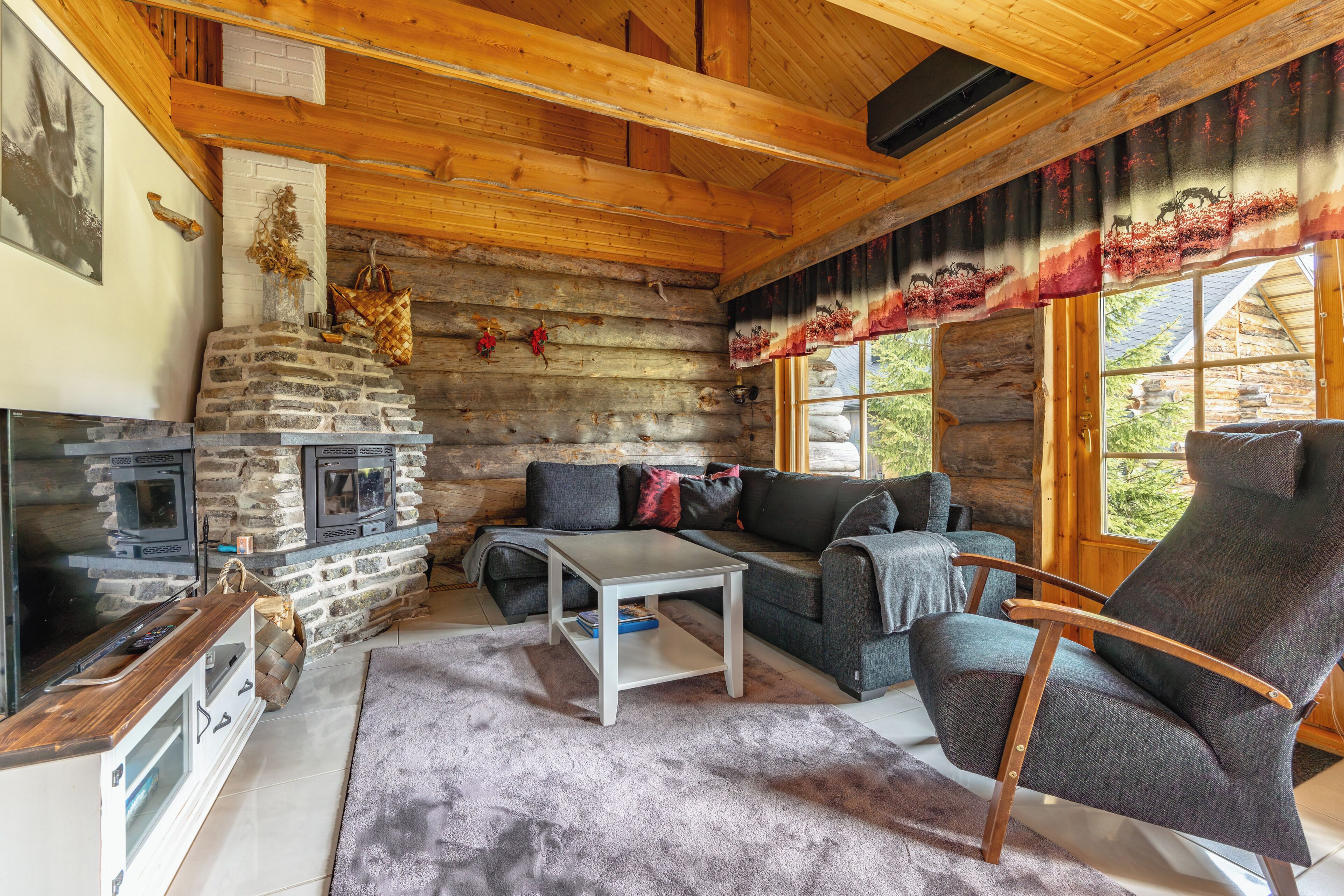 A log cabin interior with a stone fireplace, a sofa, a coffee table, and a television.