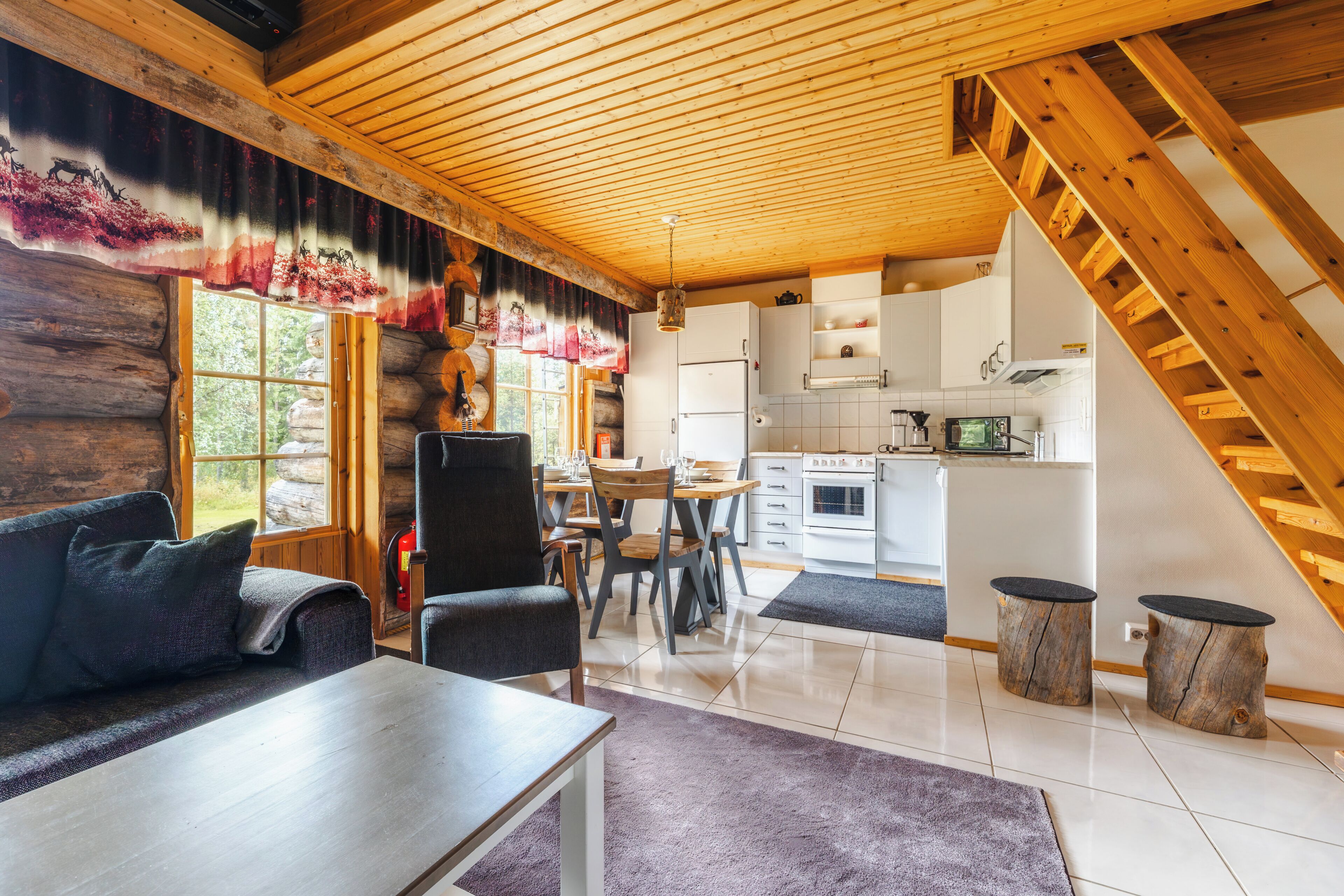 A log cabin interior with a dining area, kitchen, and a staircase.
