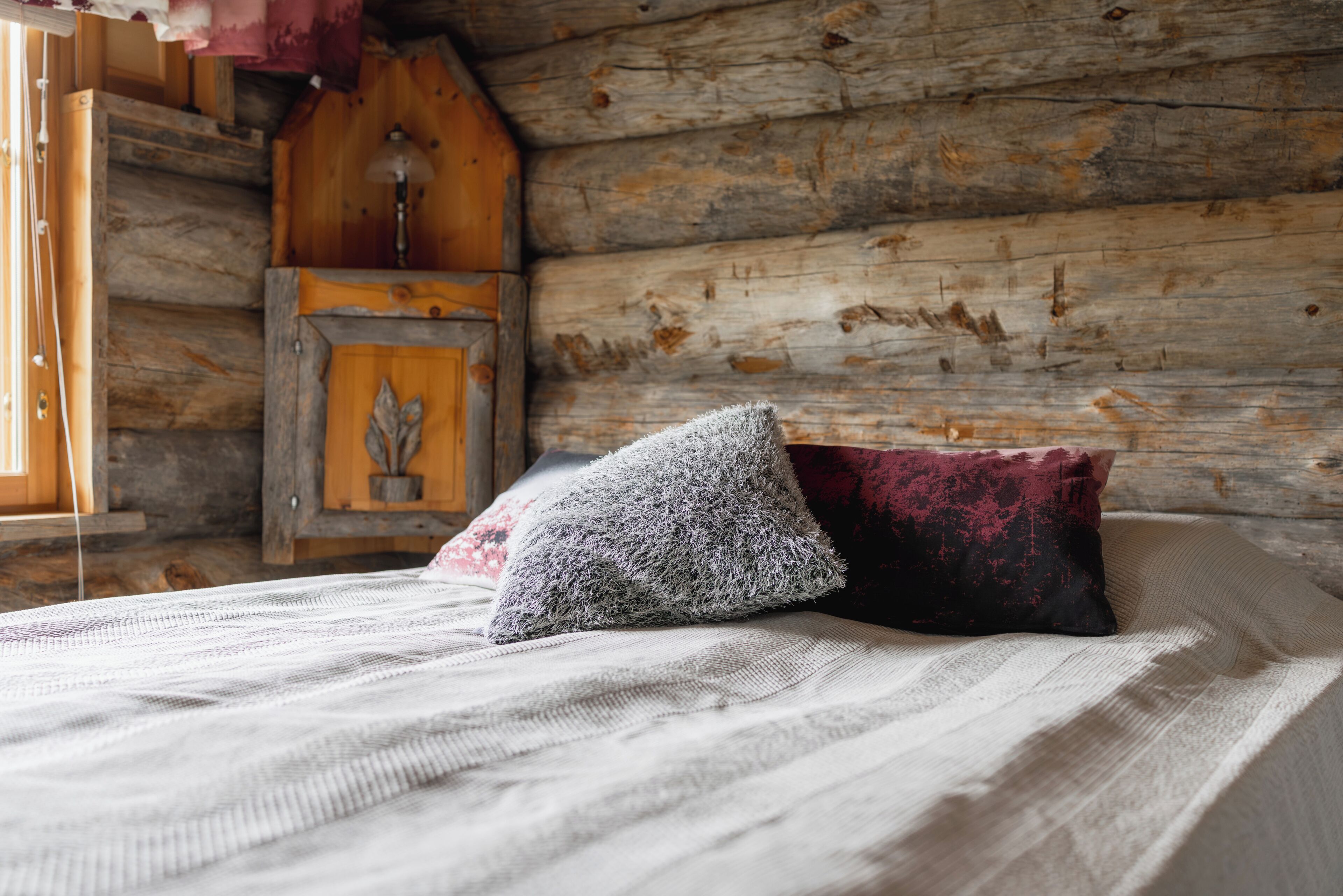 A rustic wooden interior with a bed featuring a white and a dark red pillow.