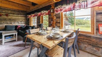 A wooden cabin interior with a dining table set for four, a sofa, and a fireplace.