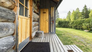 A log cabin with a wooden door, a window, and a wooden deck leading to a grassy area. - Villa Mäkitupa (Kittilä)