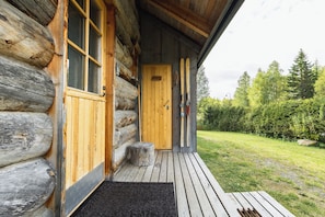 A log cabin with a wooden door, a window, and a wooden deck leading to a grassy area.