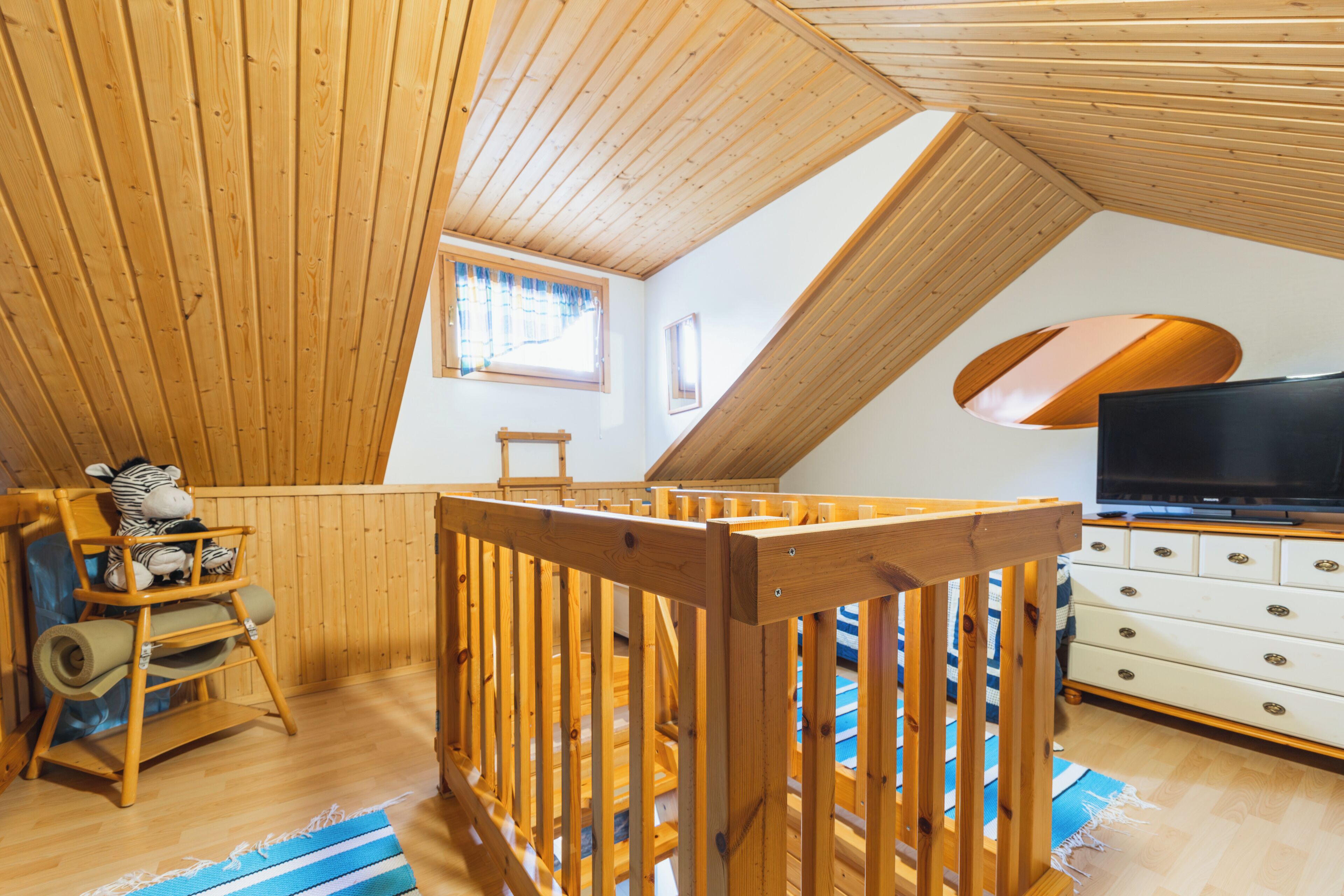 A high-ceilinged room with wooden beams, a television, and a crib.