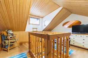 A high-ceilinged room with wooden beams, a television, and a crib.